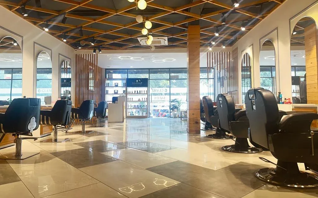 The main floor of Glamz Unisex Salon, looking towards the glass front, with barber chairs on the right and styling stations on the left under an open timber lattice ceiling